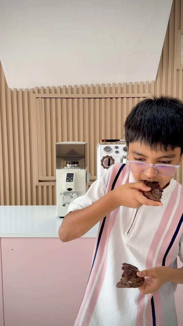 A boy in glasses biting into a brownie at the café counter