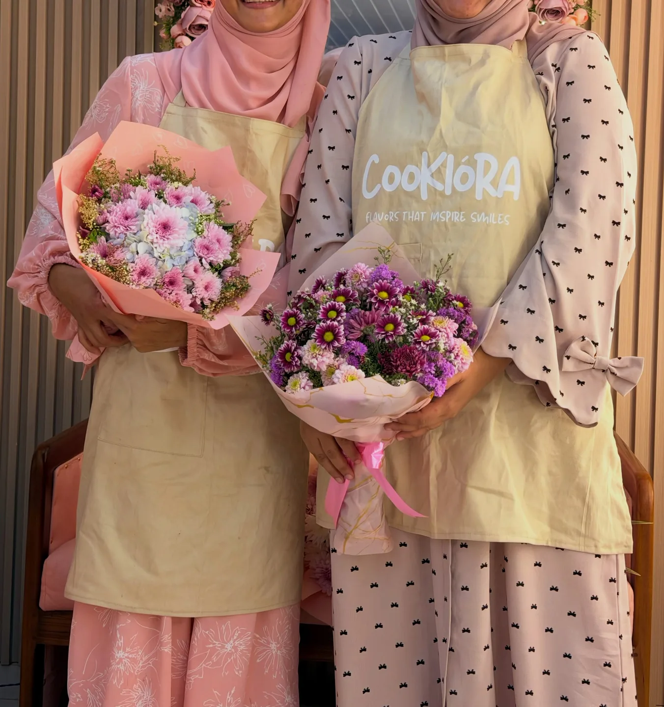Zainab and Maryam Ali in Cookiora aprons holding bouquets of flowers