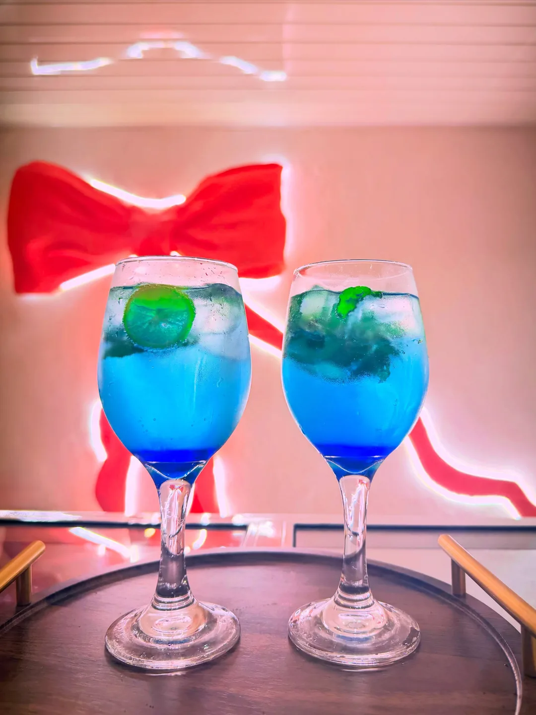 Two Blue Curaçao drinks in stemmed glasses in front of the pink bow