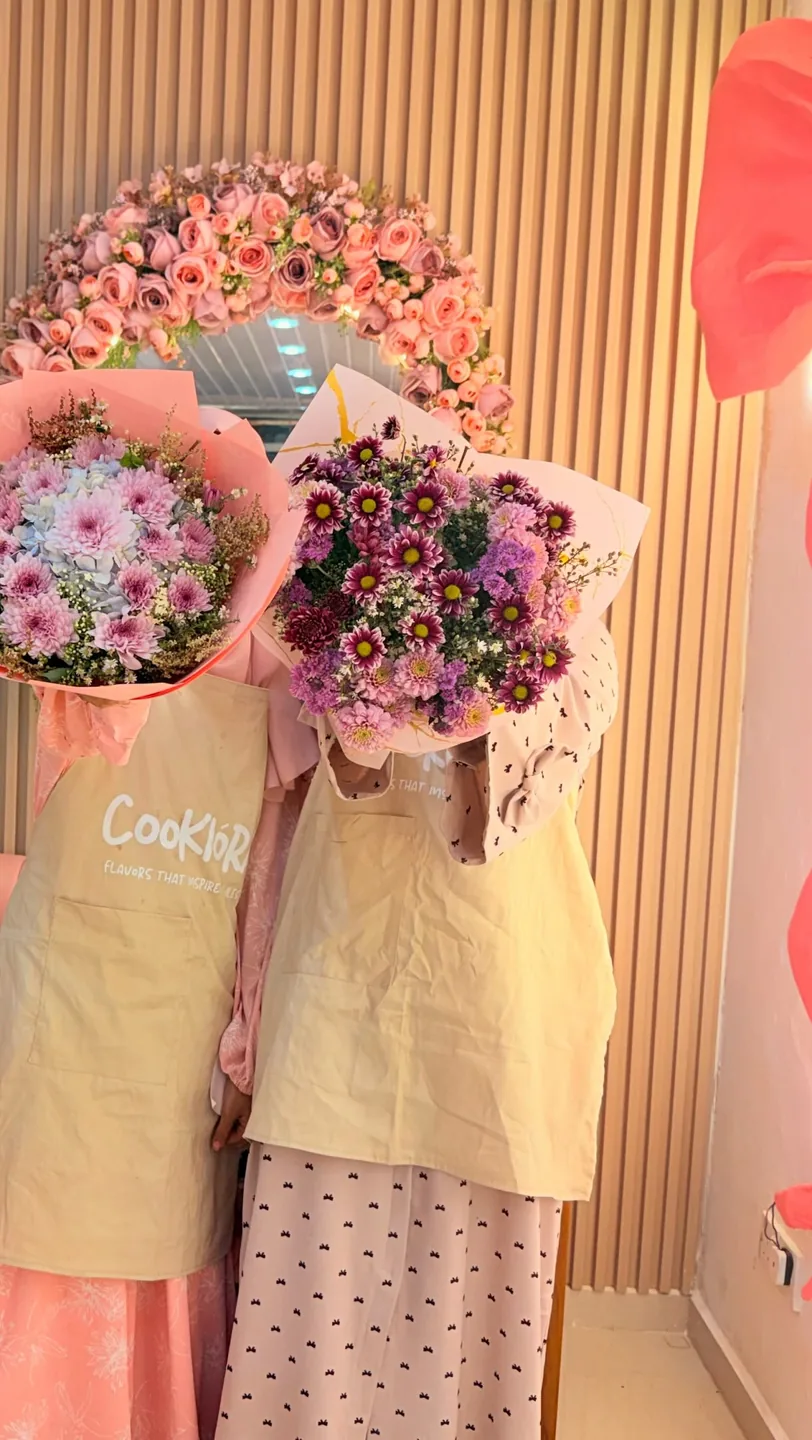 Zainab and Maryam in Cookiora aprons, faces hidden behind bouquets