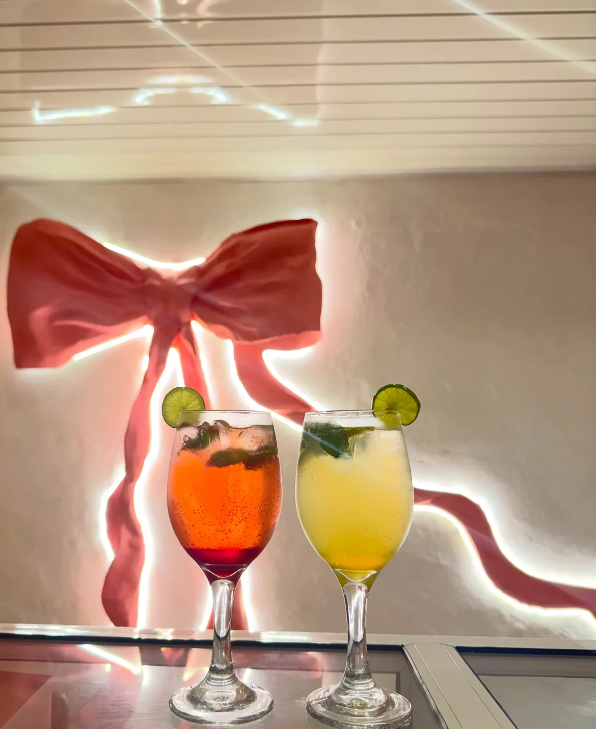 Two mojitos in stemmed glasses in front of the glowing pink bow