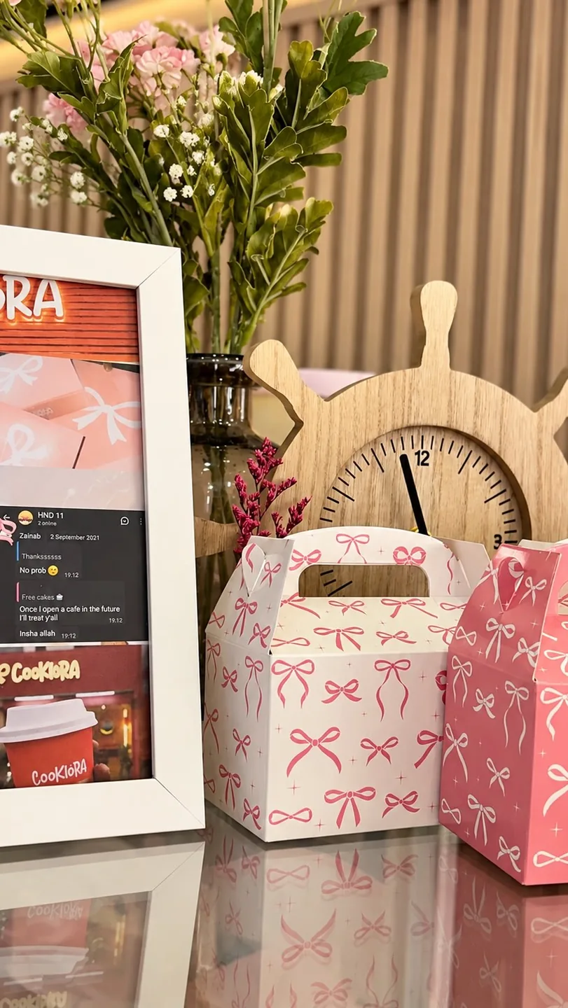 A bow-print Cookiora box next to a clock and flowers